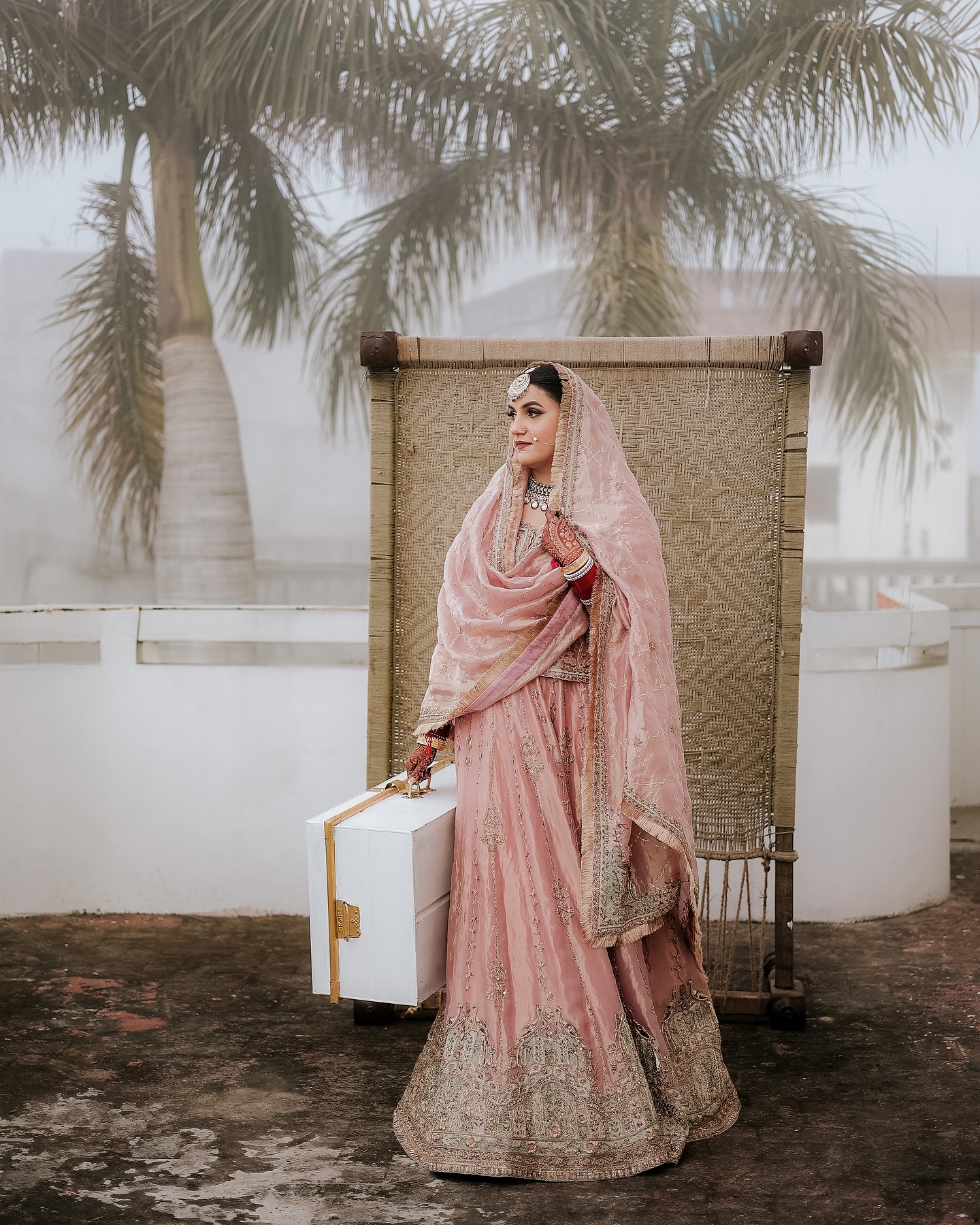 Bride in blush pink attire beside a traditional woven backdrop